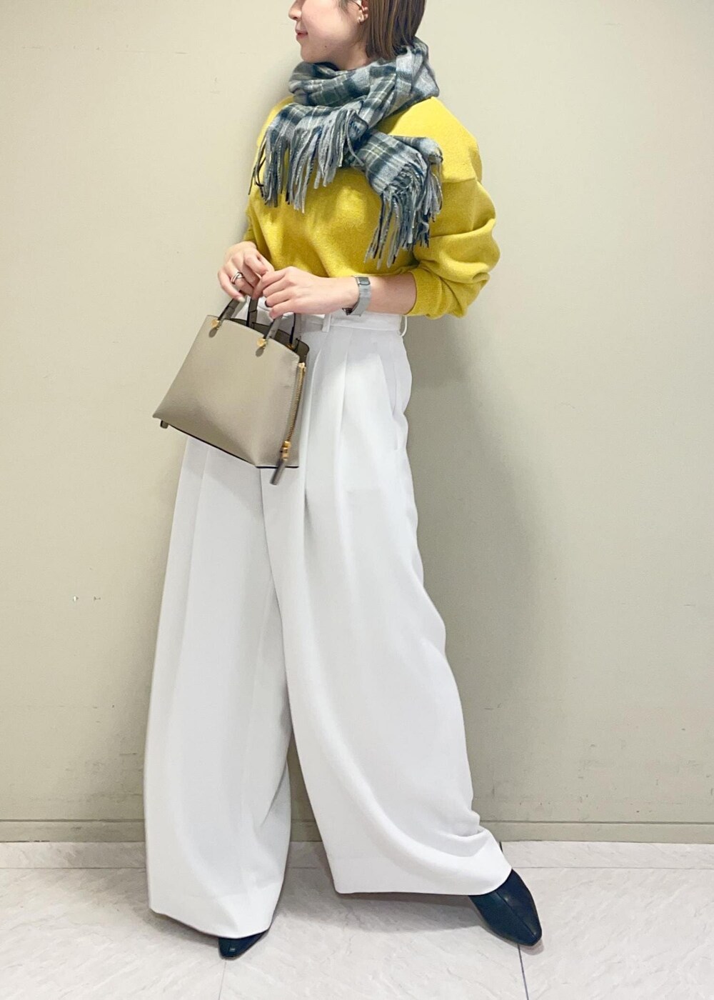 ベージュ系のハンドバッグ、ブラック系のブーツ、イエロー系のニット/セーターを着用したレディースの冬コーディネートの2枚目の写真