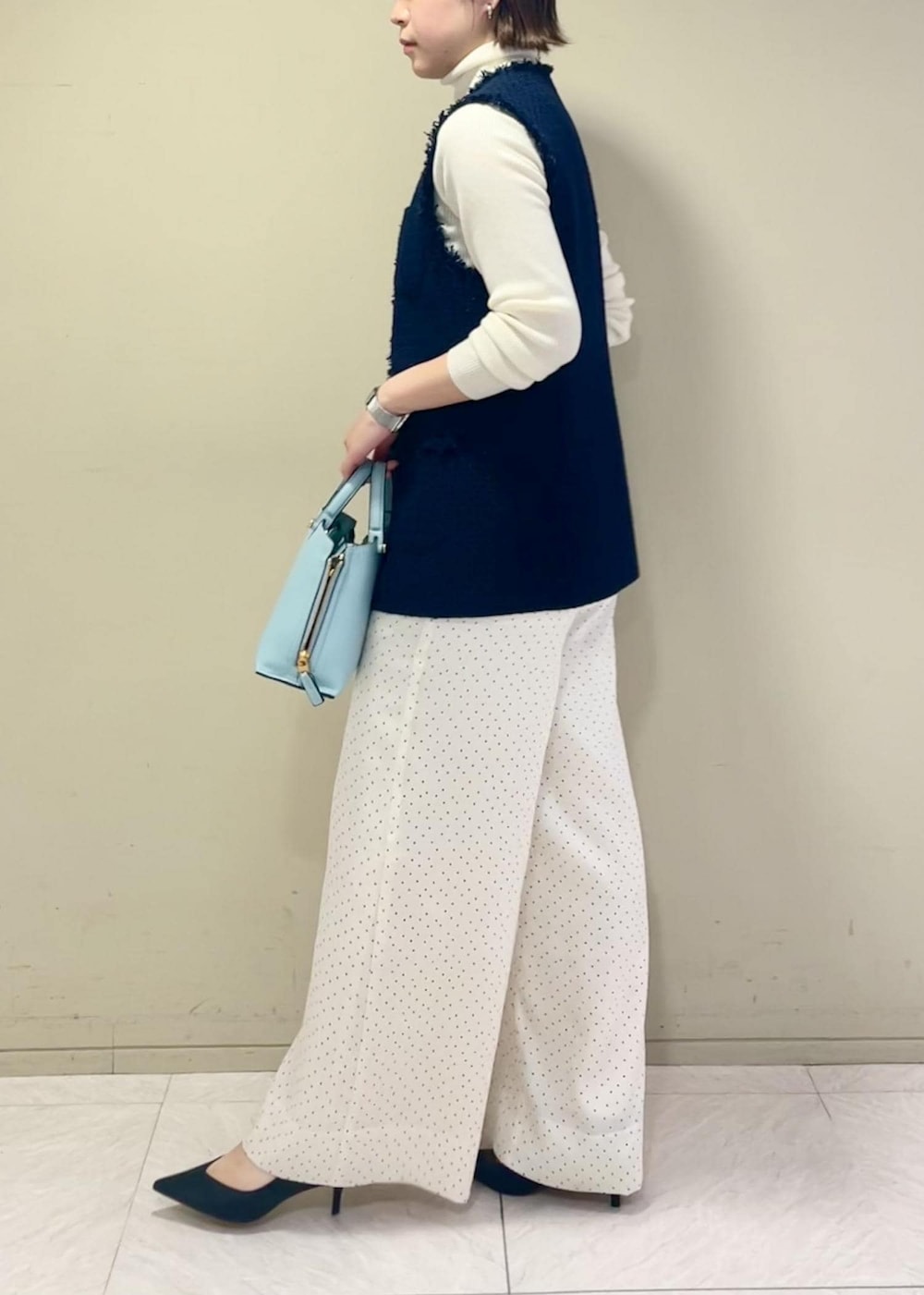 ブラック系のパンプス、ブルー系のハンドバッグ、ホワイト系のニット/セーターを着用したレディースの冬コーディネートの5枚目の写真