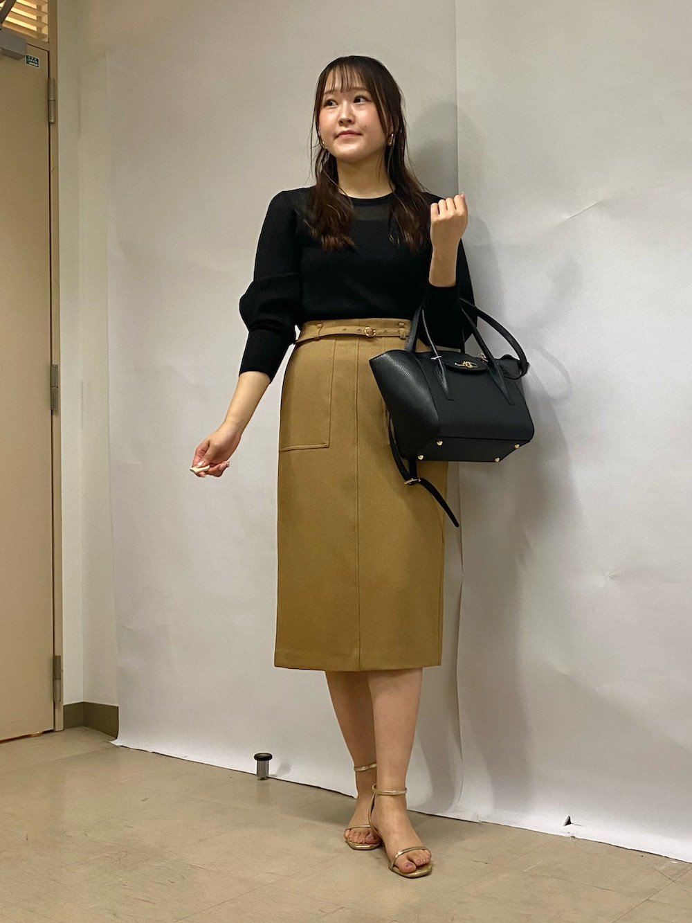 イエロー系のスカート、ブラック系のショルダーバッグ、ブラック系のニット/セーターを着用したレディースの秋コーディネートの2枚目の写真