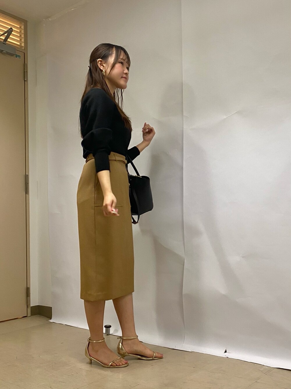 イエロー系のスカート、ブラック系のショルダーバッグ、ブラック系のニット/セーターを着用したレディースの秋コーディネートの4枚目の写真