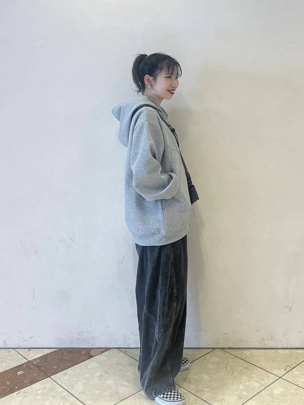 グレー系のパーカー、ブラック系のデニムパンツ、ブラック系のショルダーバッグを着用したレディースの春コーディネートの2枚目の写真