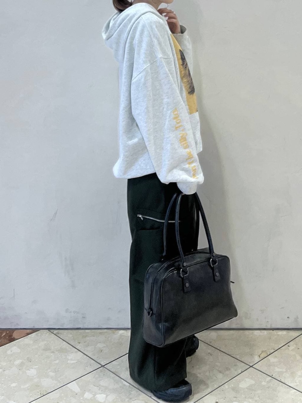 ブラック系のボストンバッグ、グリーン系のスラックス、グレー系のパーカーを着用したレディースの春コーディネートの2枚目の写真