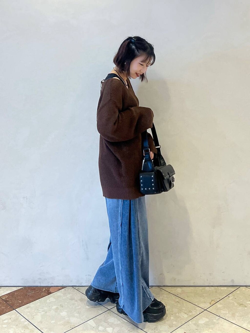 ブラック系のスニーカー、ブルー系のデニムパンツ、ブラウン系のニット/セーターを着用したレディースの夏コーディネートの2枚目の写真