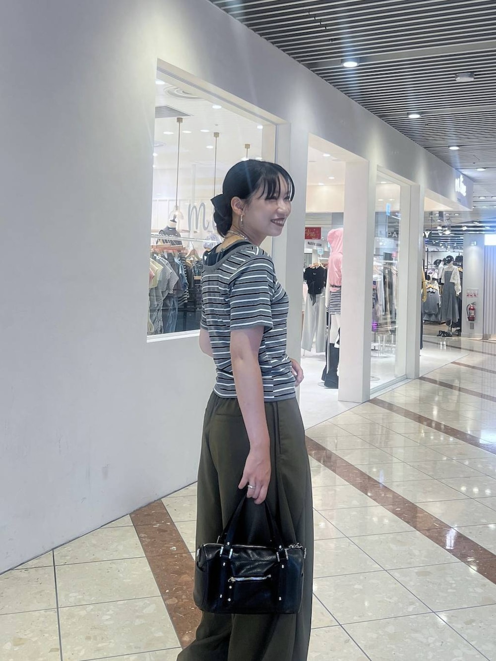 ブラック系のショルダーバッグ、グリーン系のスラックス、グレー系のTシャツ/カットソーを着用したレディースの夏コーディネートの2枚目の写真