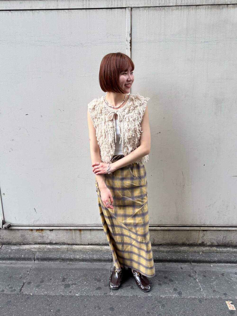 ベージュ系のベスト、イエロー系のスカート、ブラウン系のローファーを着用したレディースの夏コーディネートの4枚目の写真