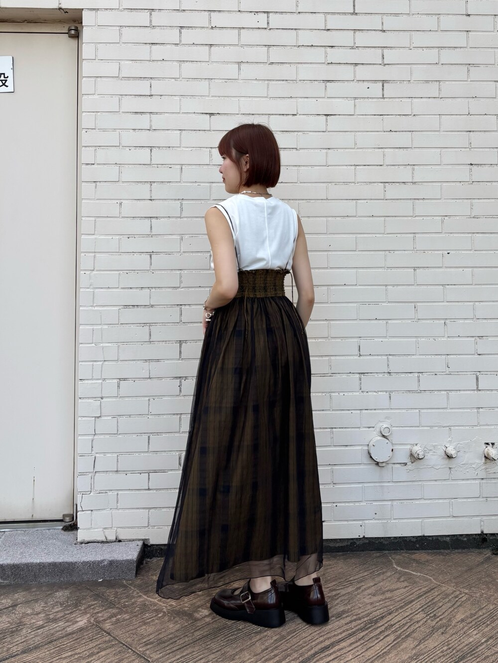 グリーン系のスカート、ホワイト系のTシャツ/カットソー、ブラウン系のスニーカーを着用したレディースの夏コーディネートの2枚目の写真