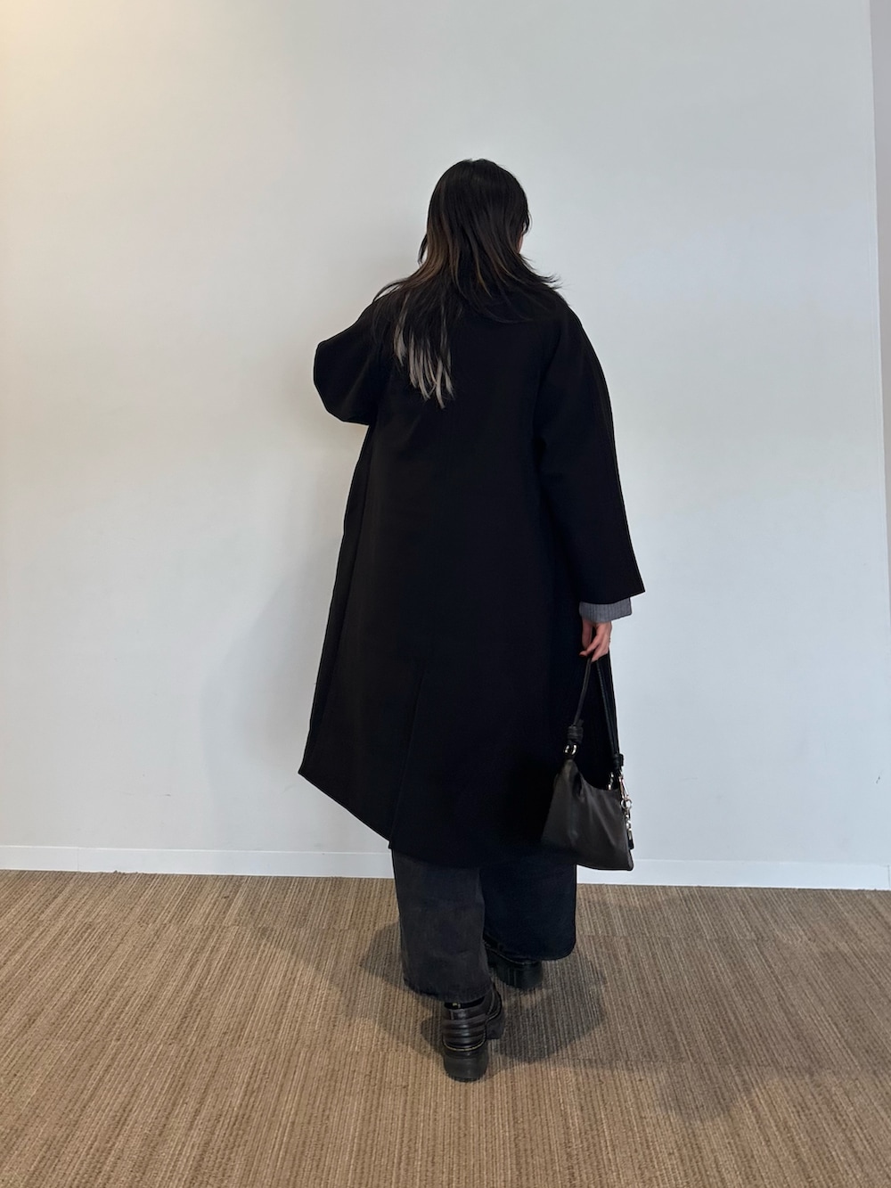 ブラック系のチェスターコート、ホワイト系のTシャツ/カットソー、グレー系のニット/セーターを着用したレディースの冬コーディネートの3枚目の写真