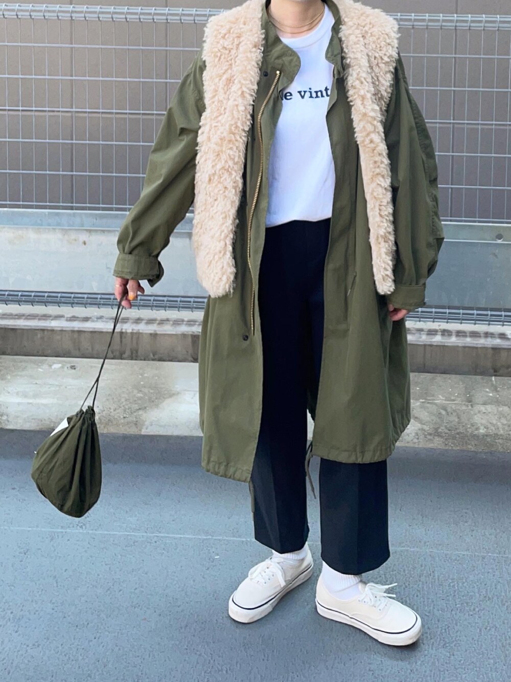 グリーン系のモッズコート、ベージュ系のベスト、ホワイト系のスニーカーを着用したレディースの秋コーディネートの2枚目の写真