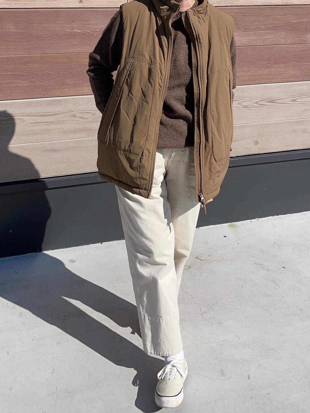 ブラウン系のベスト、ホワイト系のデニムパンツ、ホワイト系のスニーカーを着用したレディースの秋コーディネートの2枚目の写真