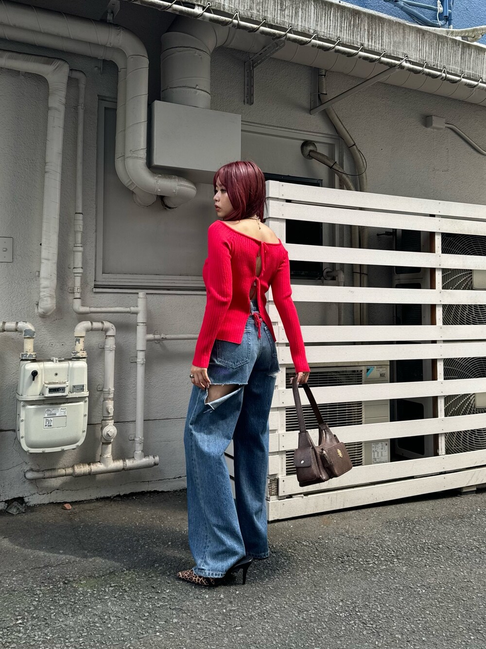レッド系のニット/セーター、ブルー系のデニムパンツ、ブラウン系のハンドバッグを着用したレディースの夏コーディネートの3枚目の写真
