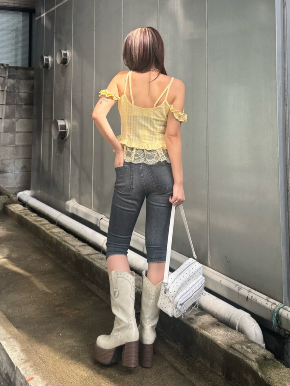 ホワイト系のハンドバッグ、イエロー系のキャミソール、ブラック系のデニムパンツを着用したレディースの春コーディネートの3枚目の写真