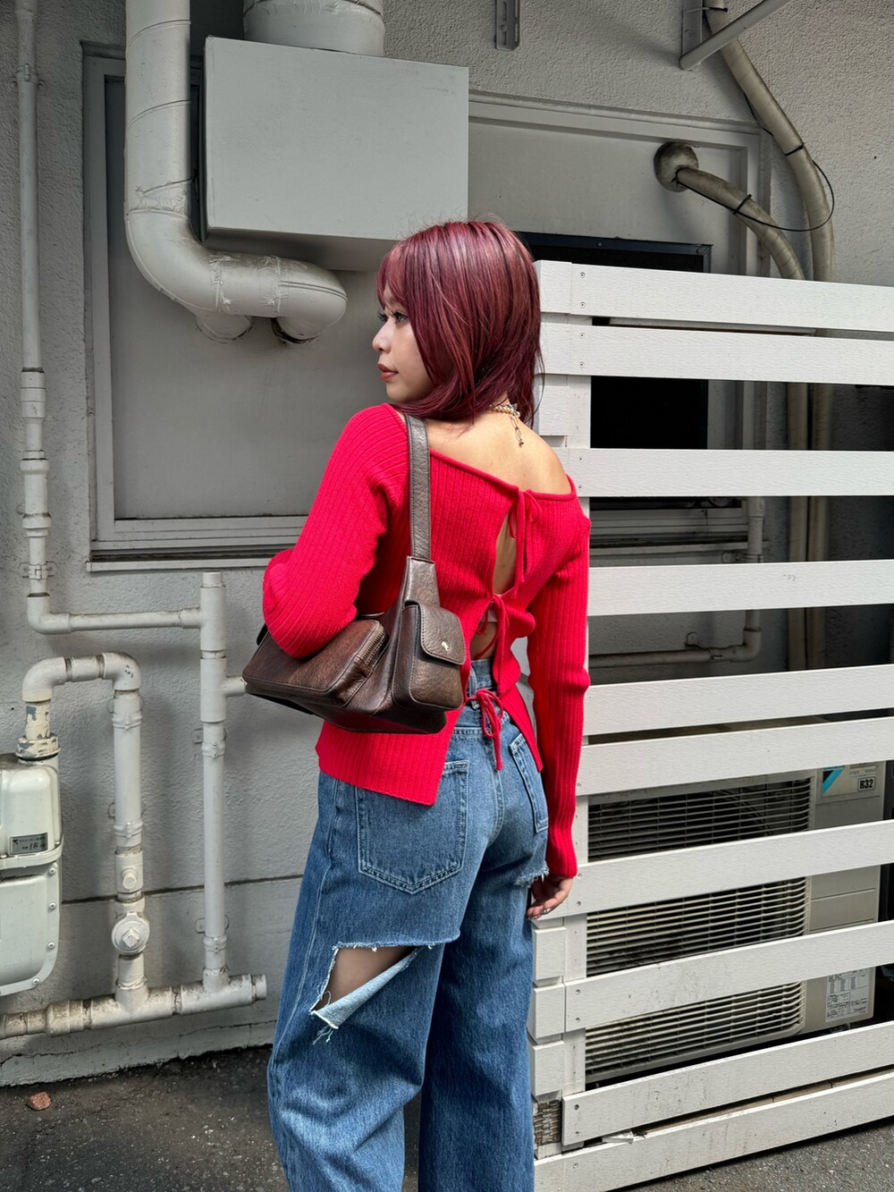 レッド系のニット/セーター、ブルー系のデニムパンツ、ブラウン系のハンドバッグを着用したレディースの夏コーディネートの2枚目の写真