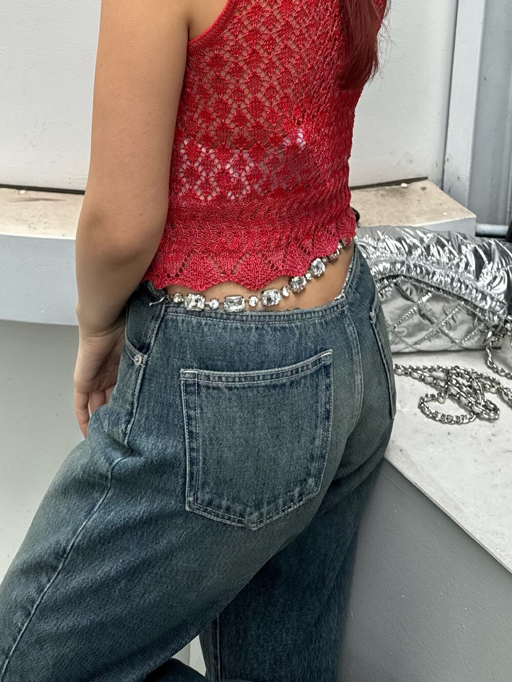 レッド系のニット/セーター、ブルー系のデニムパンツ、シルバー系のショルダーバッグを着用したレディースの春コーディネートの3枚目の写真