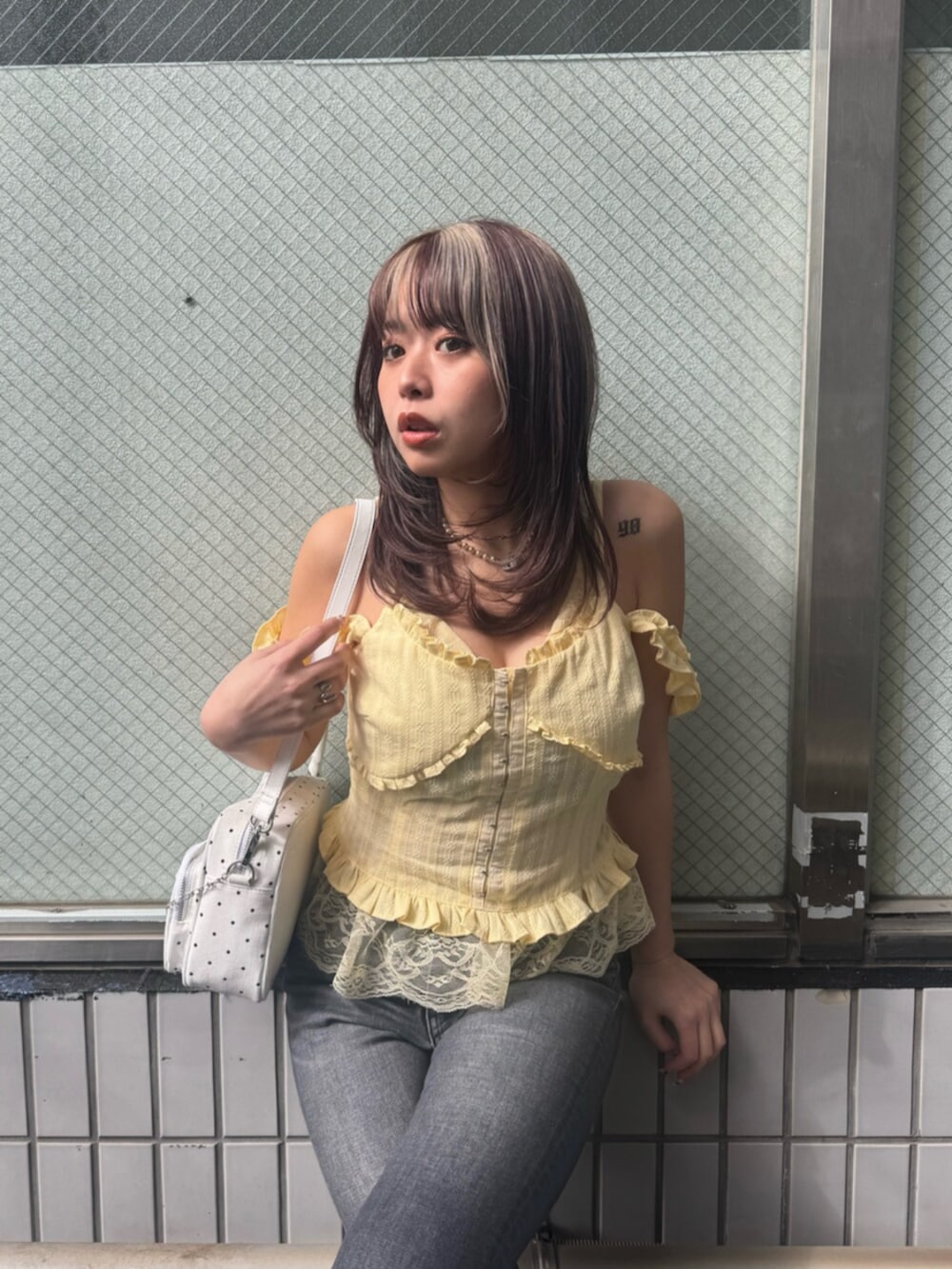 ホワイト系のハンドバッグ、イエロー系のキャミソール、ブラック系のデニムパンツを着用したレディースの春コーディネートの4枚目の写真