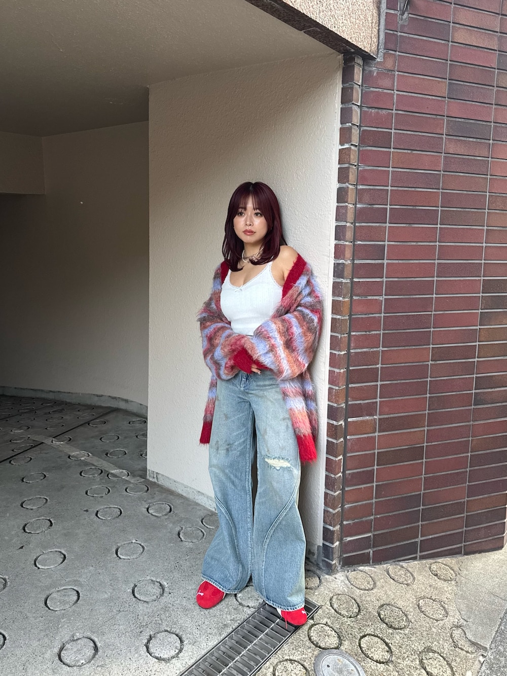 レッド系のカーディガン/ボレロ、ブルー系のデニムパンツ、レッド系のスニーカーを着用したレディースの冬コーディネートの2枚目の写真