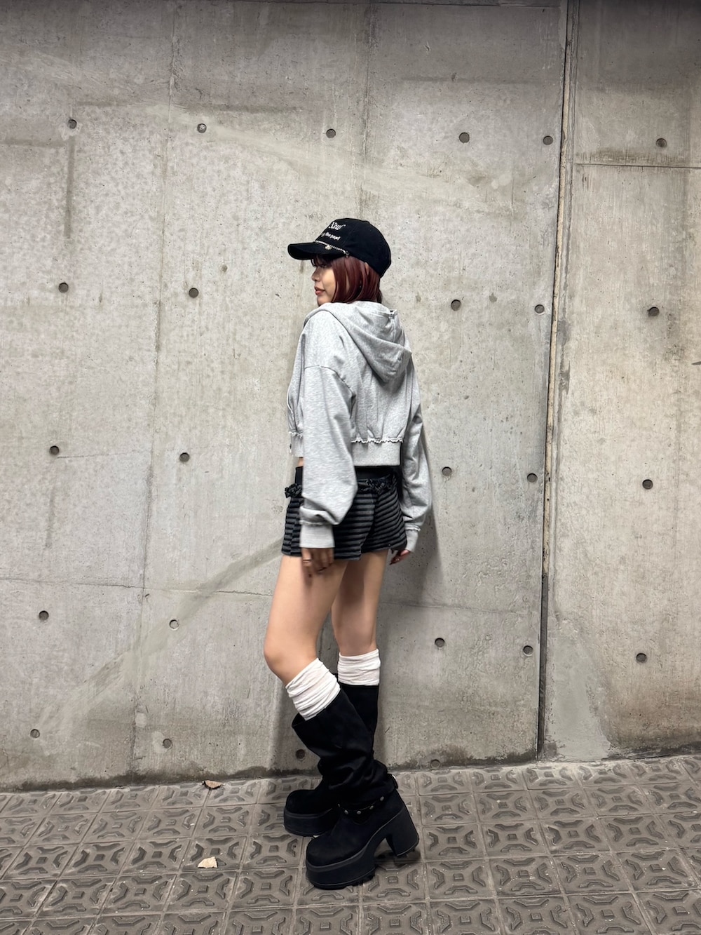 グレー系のパーカー、ブラック系のブーツ、ブラック系のキャップを着用したレディースの秋コーディネートの2枚目の写真