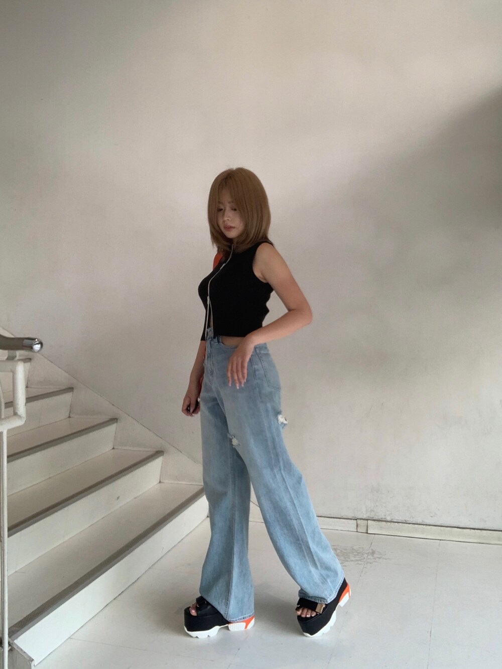 ブラック系のタンクトップ、ブルー系のデニムパンツ、オレンジ系のショルダーバッグを着用したレディースの夏コーディネートの2枚目の写真