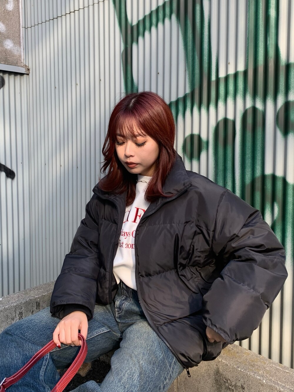 ブルー系のデニムパンツ、レッド系のショルダーバッグ、ブラック系のダウンジャケット/コートを着用したレディースの冬コーディネートの2枚目の写真