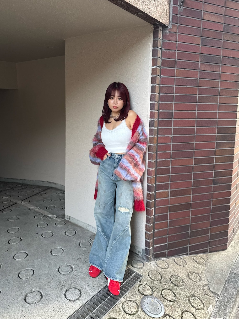 レッド系のカーディガン/ボレロ、ブルー系のデニムパンツ、レッド系のスニーカーを着用したレディースの冬コーディネートの3枚目の写真