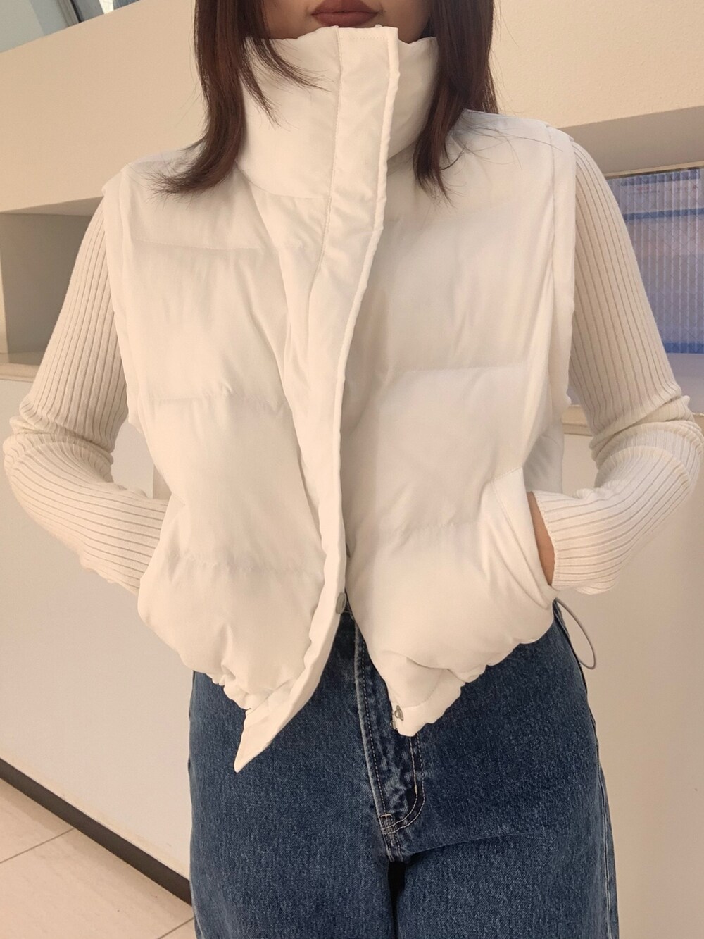 ホワイト系のダウンベスト、ホワイト系のニット/セーター、ブルー系のデニムパンツを着用したレディースの秋コーディネートの3枚目の写真