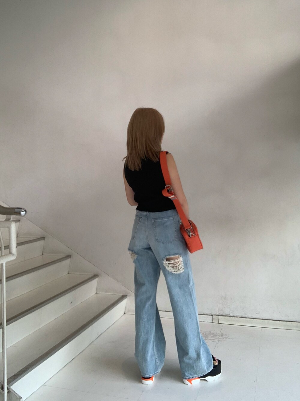 ブラック系のタンクトップ、ブルー系のデニムパンツ、オレンジ系のショルダーバッグを着用したレディースの夏コーディネートの3枚目の写真