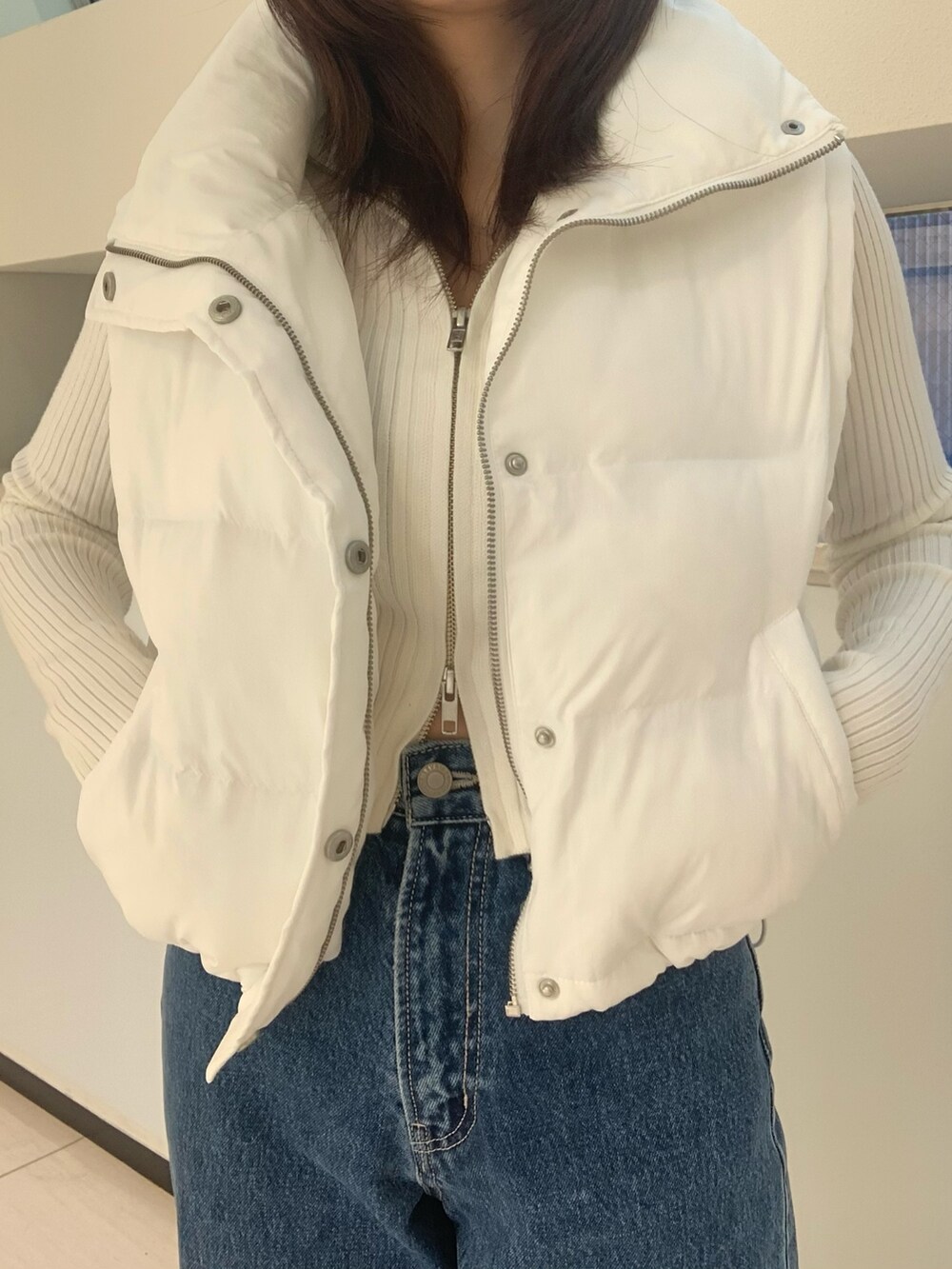 ホワイト系のダウンベスト、ホワイト系のニット/セーター、ブルー系のデニムパンツを着用したレディースの秋コーディネートの4枚目の写真