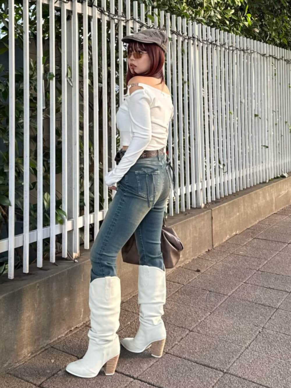 ブラウン系のボストンバッグ、ホワイト系のブーツ、ブルー系のデニムパンツを着用したレディースの春コーディネートの2枚目の写真