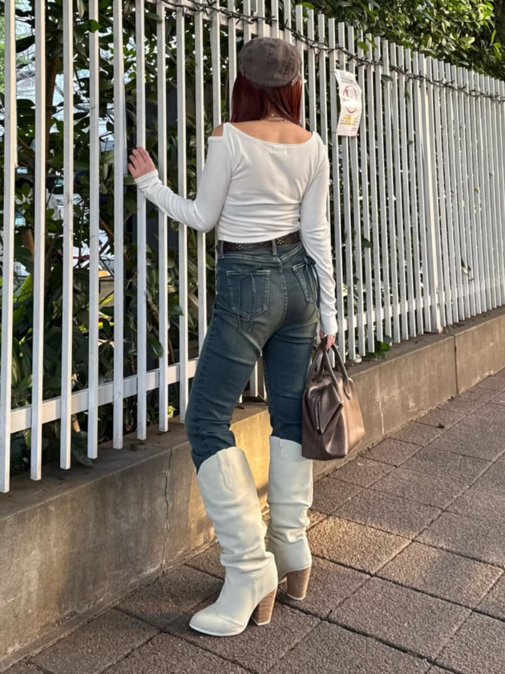 ブラウン系のボストンバッグ、ホワイト系のブーツ、ブルー系のデニムパンツを着用したレディースの春コーディネートの3枚目の写真