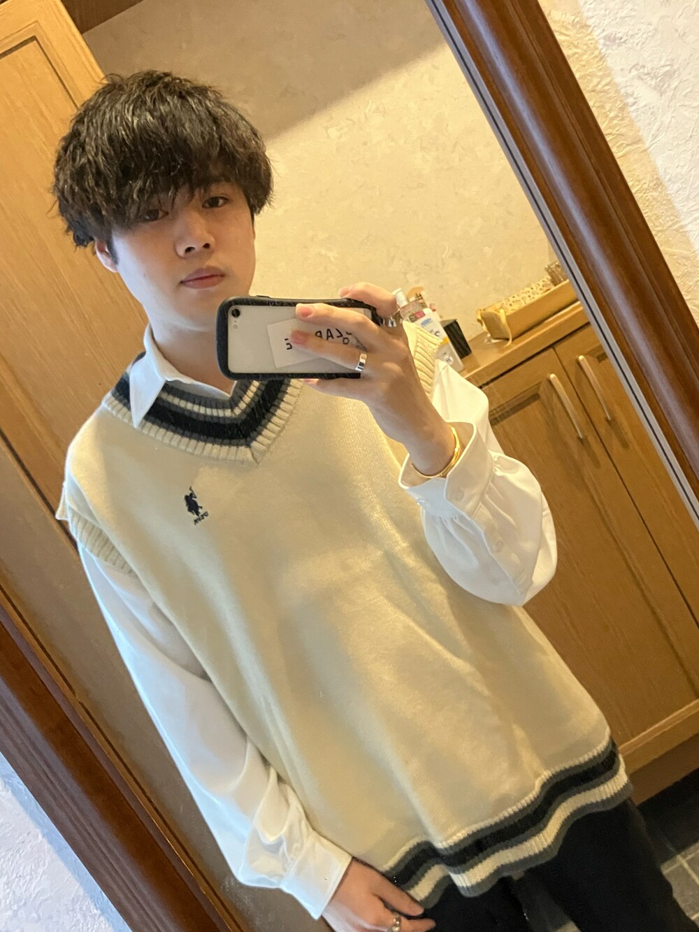 ブラック系のスニーカー、ブラック系のデニムパンツ、ホワイト系のベストを着用したメンズの春コーディネートの2枚目の写真