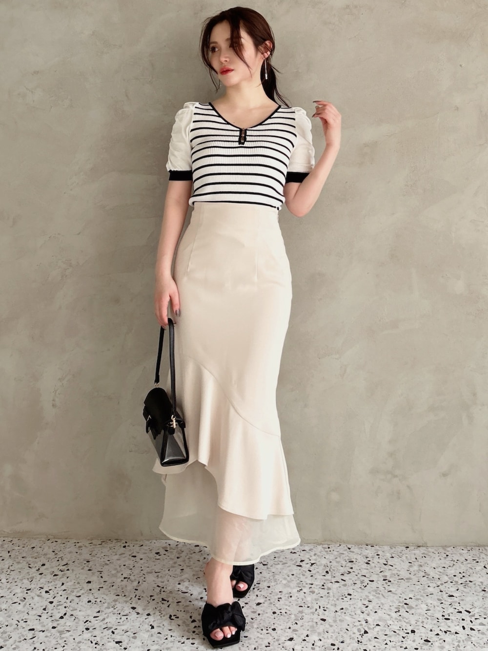 ホワイト系のスカート、その他のニット/セーター、ブラック系のハンドバッグを着用したレディースの春コーディネートの2枚目の写真