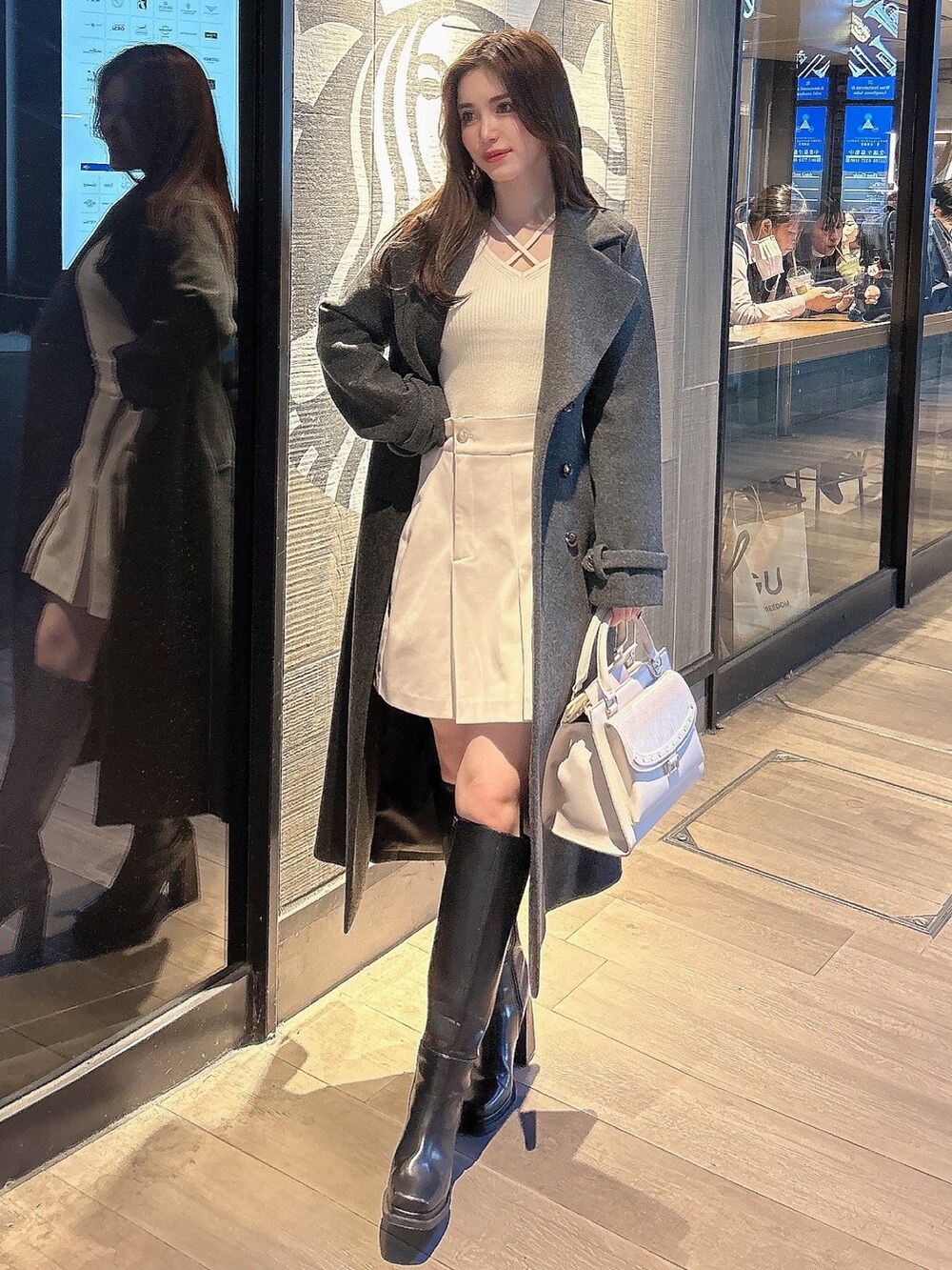 グレー系のチェスターコート、ブラック系のブーツ、ホワイト系のハンドバッグを着用したレディースの秋コーディネートの4枚目の写真