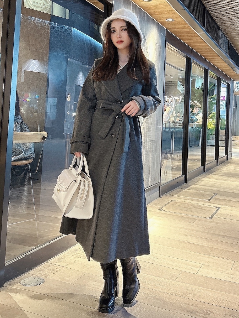 グレー系のチェスターコート、ブラック系のブーツ、ホワイト系のハンドバッグを着用したレディースの秋コーディネートの2枚目の写真