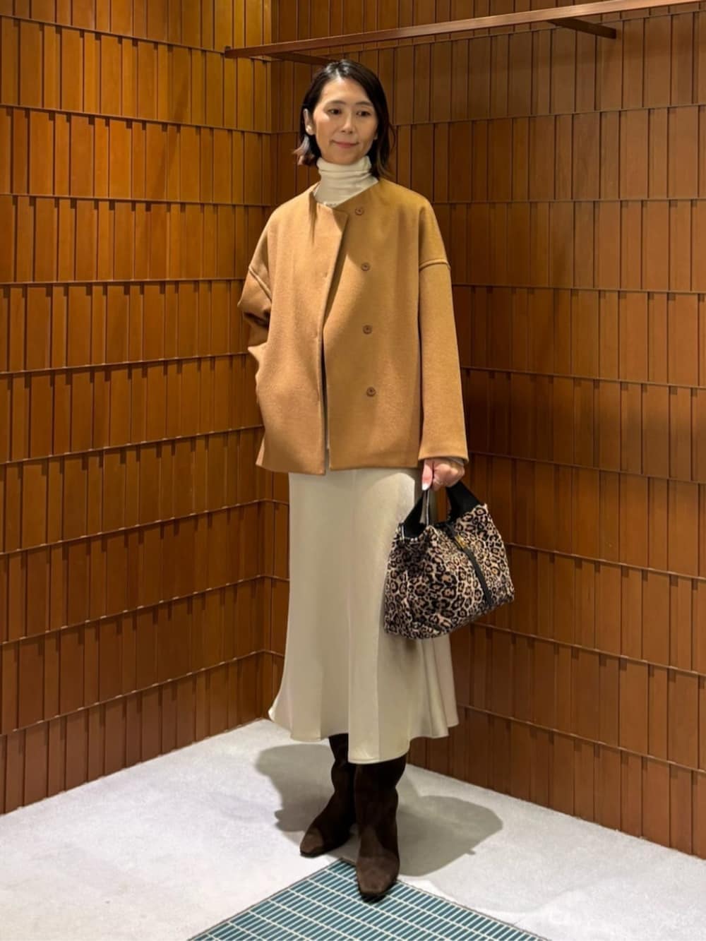イエロー系のノーカラーコート、ホワイト系のニット/セーター、ベージュ系のスカートを着用したレディースの秋コーディネートの2枚目の写真
