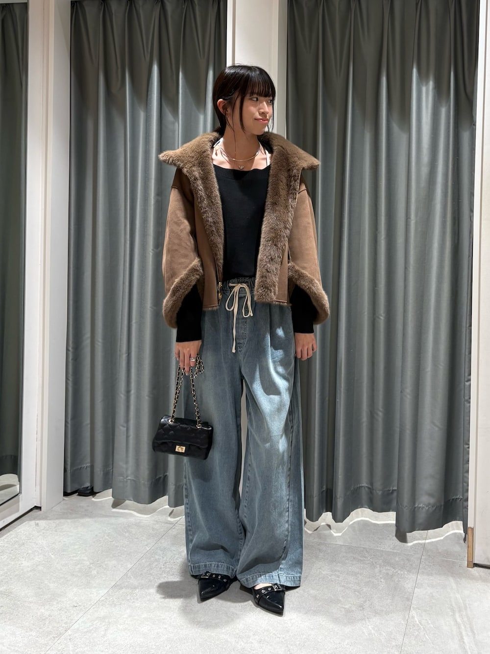 ブラウン系のその他アウター、ブラック系のニット/セーター、ブルー系のデニムパンツを着用したレディースの秋コーディネートの2枚目の写真