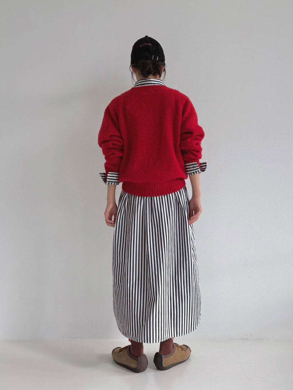 レッド系のニット/セーター、ブラック系のシャツワンピース、ブラウン系のモカシン/デッキシューズを着用したレディースの秋コーディネートの3枚目の写真