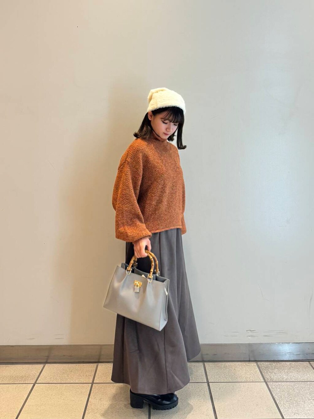 グレー系のハンドバッグ、グレー系のスカート、オレンジ系のニット/セーターを着用したレディースの冬コーディネートの2枚目の写真