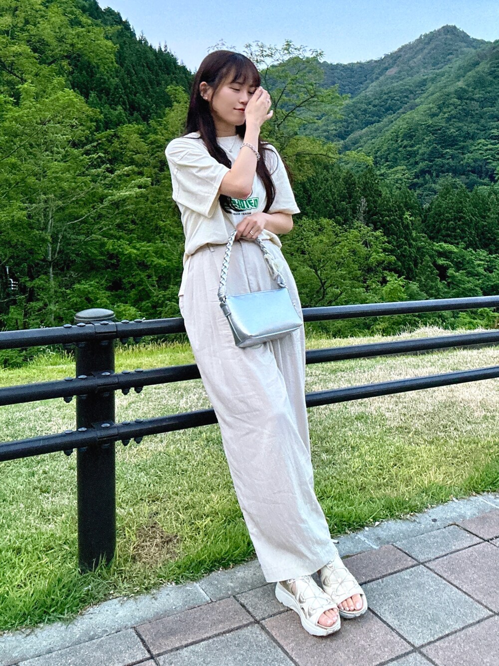 シルバー系のショルダーバッグ、ホワイト系のTシャツ/カットソー、ブラック系のサンダルを着用したレディースの夏コーディネートの2枚目の写真