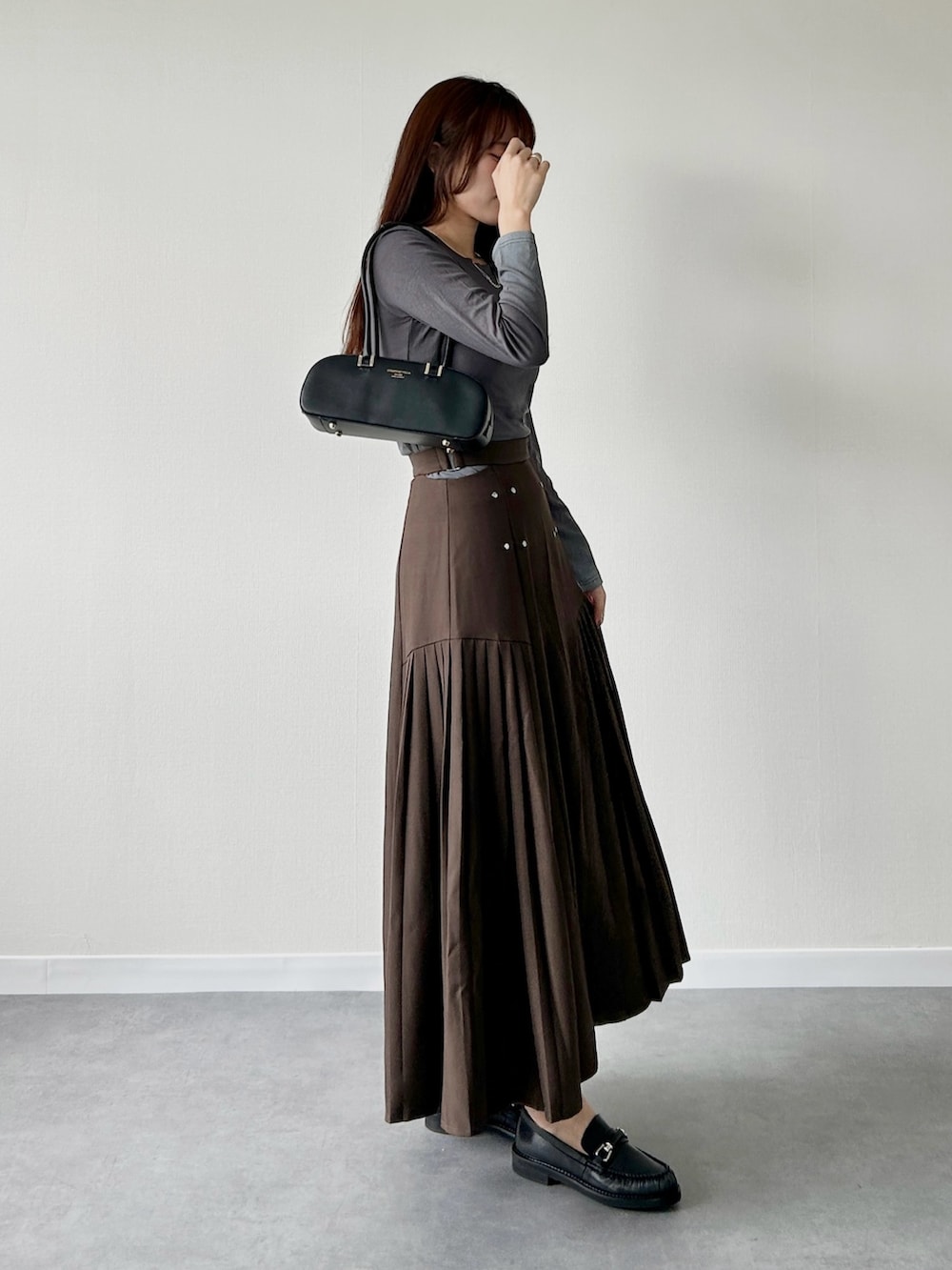 ブラウン系のスカート、ブラウン系のローファー、レッド系のショルダーバッグを着用したレディースの秋コーディネートの2枚目の写真