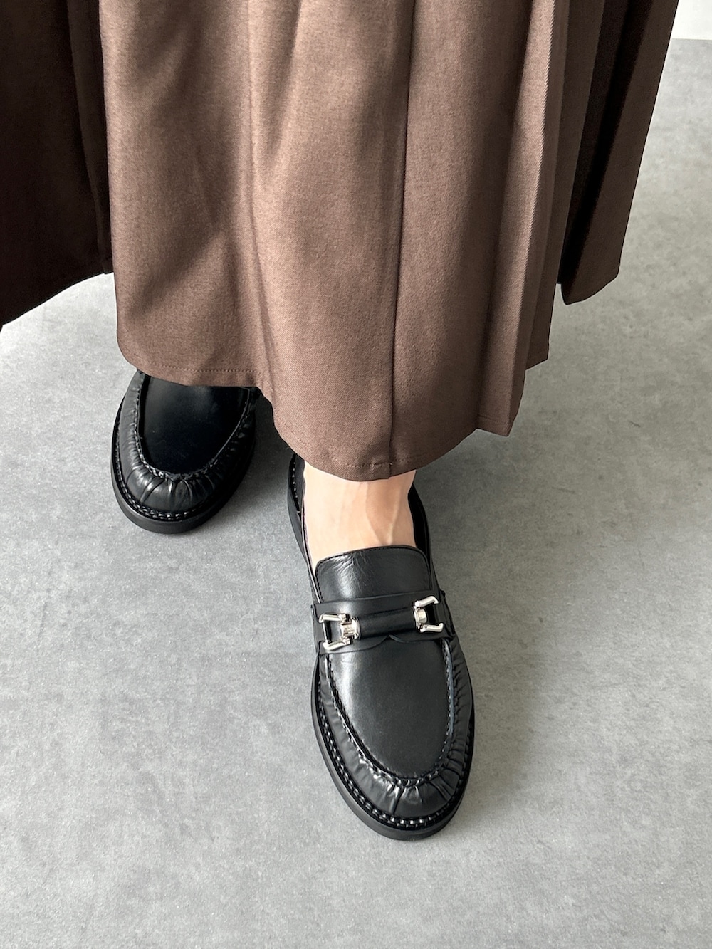 ブラウン系のスカート、ブラウン系のローファー、レッド系のショルダーバッグを着用したレディースの秋コーディネートの4枚目の写真