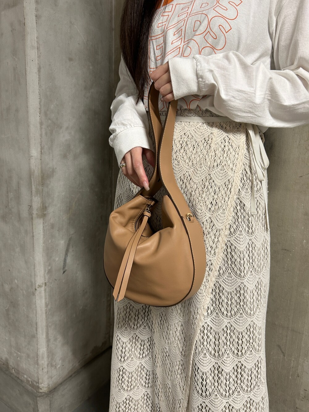 ホワイト系のTシャツ/カットソー、ベージュ系のハンドバッグ、ブラック系のパンプスを着用したレディースの春コーディネートの2枚目の写真