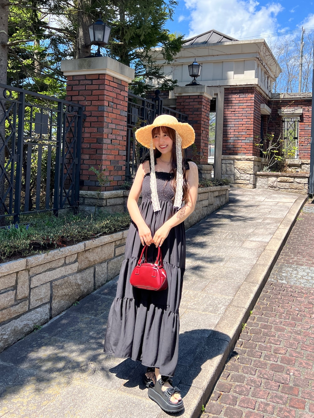 ブラック系のワンピース、レッド系のトートバッグ、ブラック系のサンダルを着用したレディースの夏コーディネートの2枚目の写真