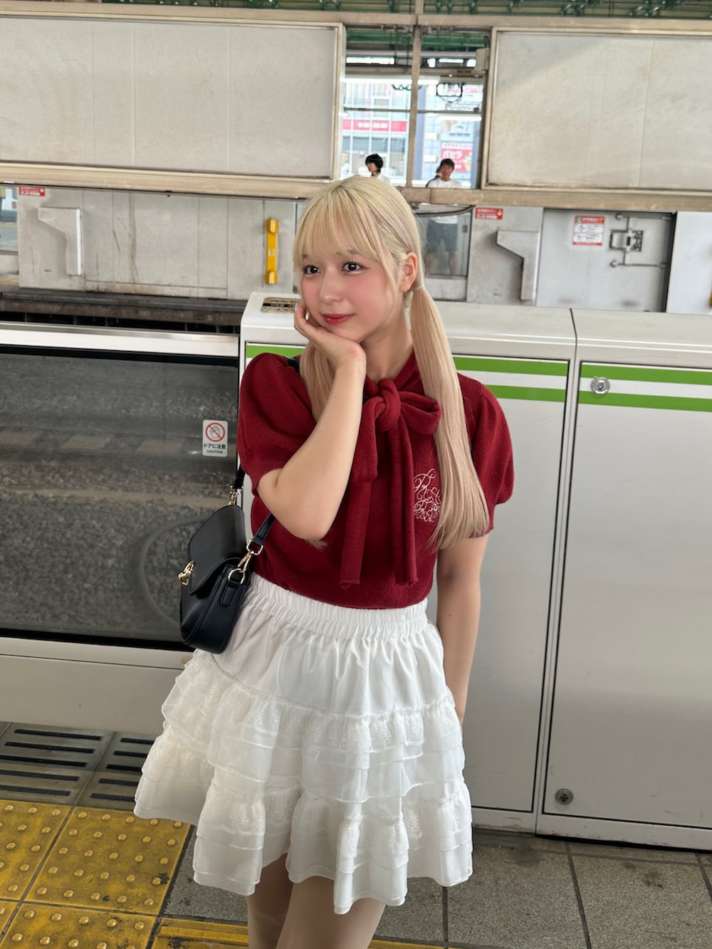 レッド系のニット/セーター、ホワイト系のスカート、ブラック系のショルダーバッグを着用したレディースの夏コーディネートの2枚目の写真