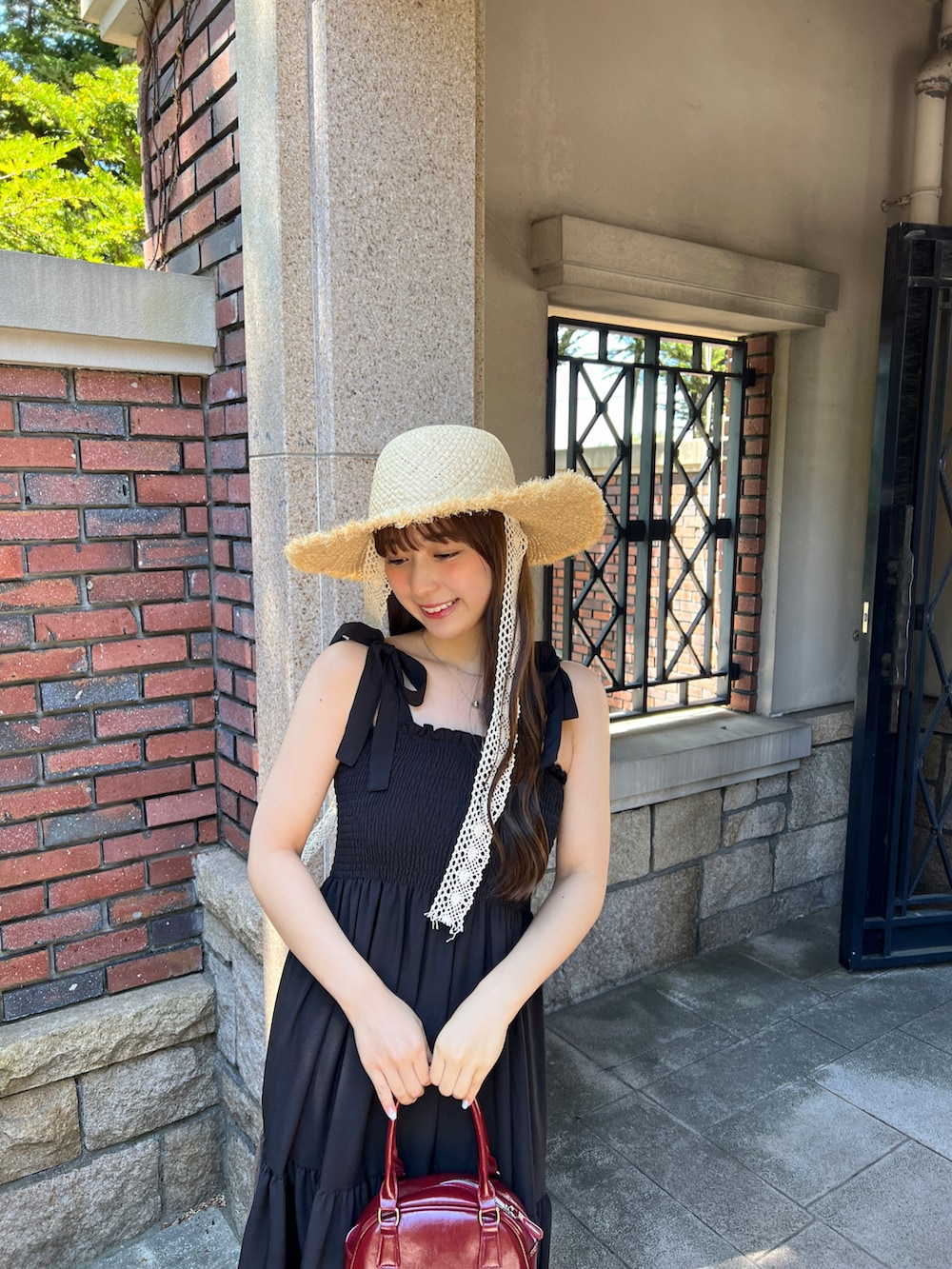 ブラック系のワンピース、レッド系のトートバッグ、ブラック系のサンダルを着用したレディースの夏コーディネートの4枚目の写真