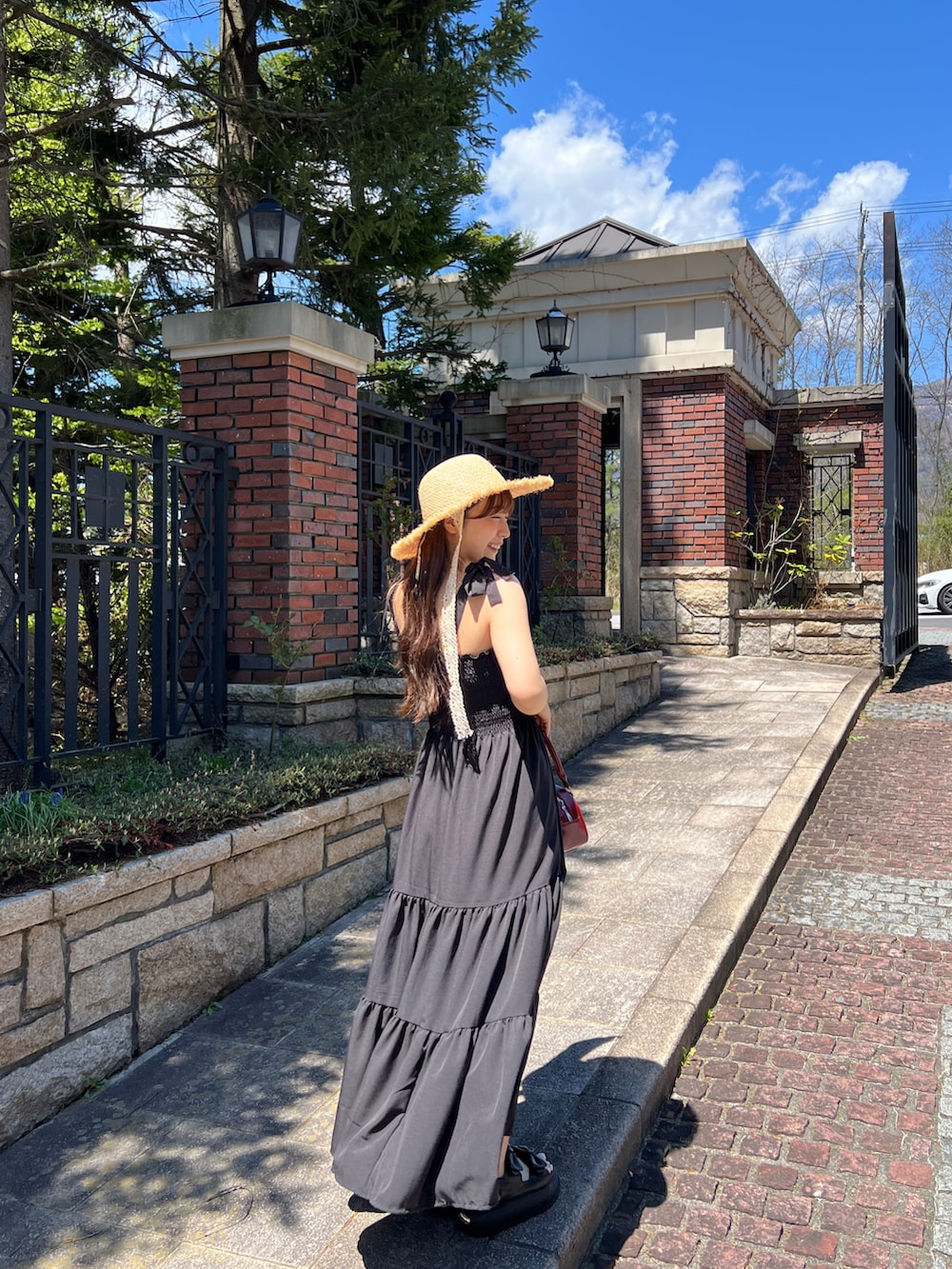 ブラック系のワンピース、レッド系のトートバッグ、ブラック系のサンダルを着用したレディースの夏コーディネートの3枚目の写真