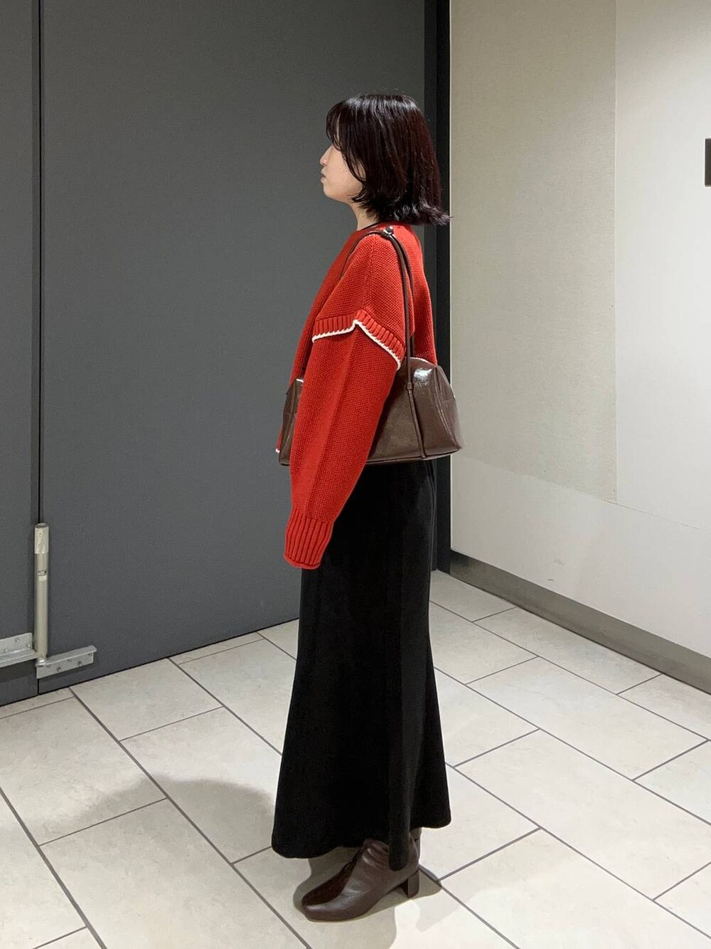 レッド系のニット/セーター、ブラック系のスカート、ブラウン系のボストンバッグを着用したレディースの秋コーディネートの2枚目の写真
