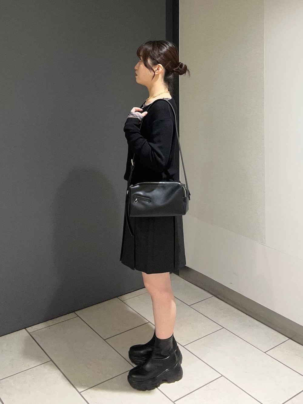 ブラック系のブーツ、グレー系のスカート、ブラック系のショルダーバッグを着用したレディースの秋コーディネートの2枚目の写真