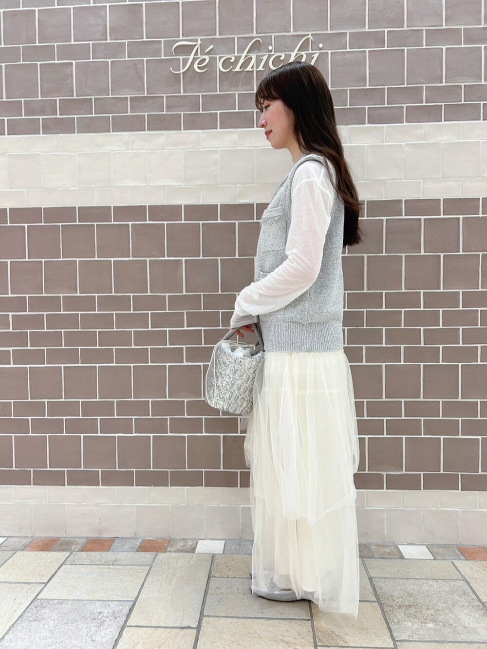 グレー系のニット/セーター、ホワイト系のTシャツ/カットソー、ホワイト系のスカートを着用したレディースの春コーディネートの2枚目の写真