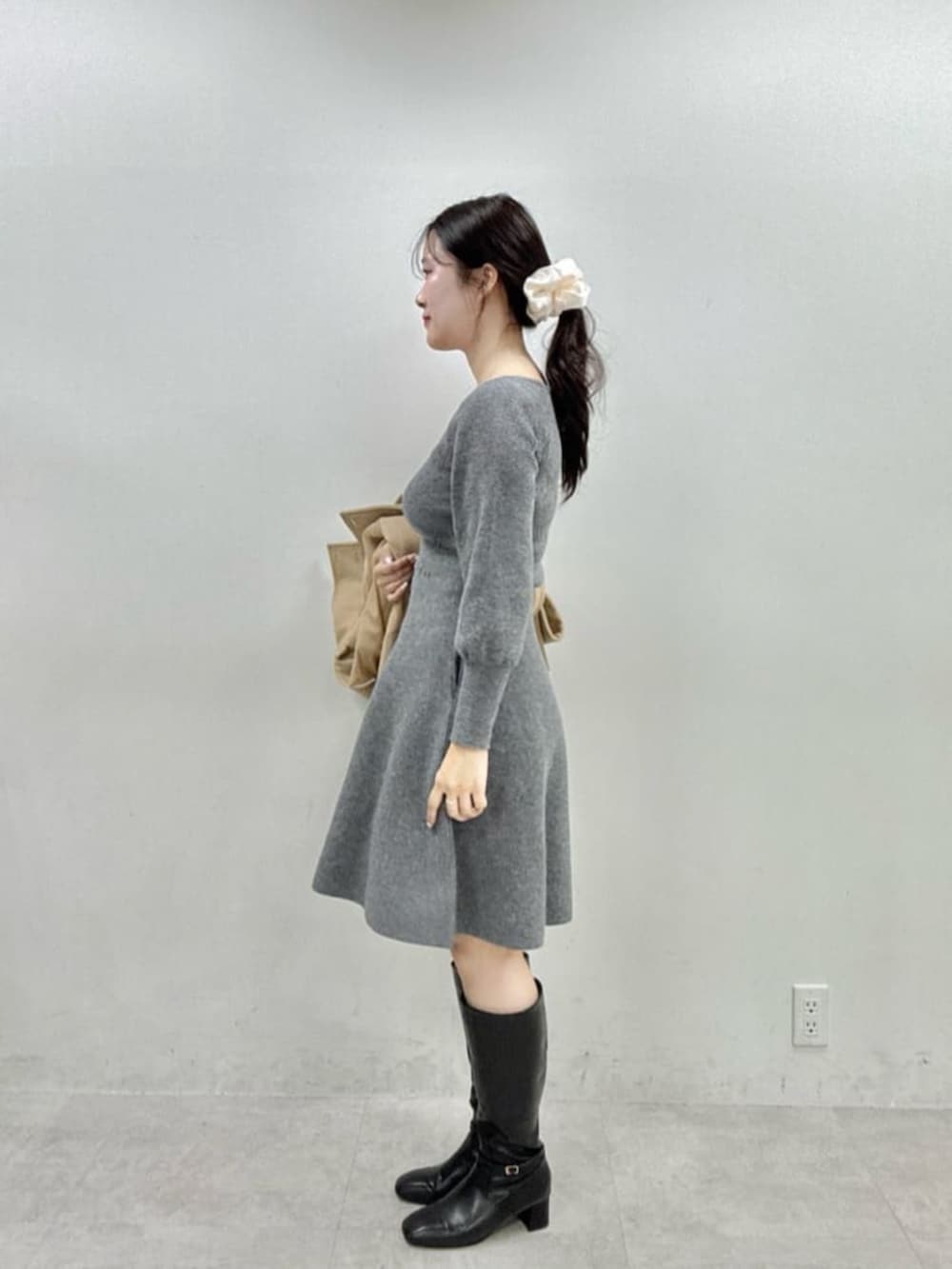 ブラック系のブーツ、ベージュ系のその他アウター、グレー系のワンピースを着用したレディースの秋コーディネートの2枚目の写真