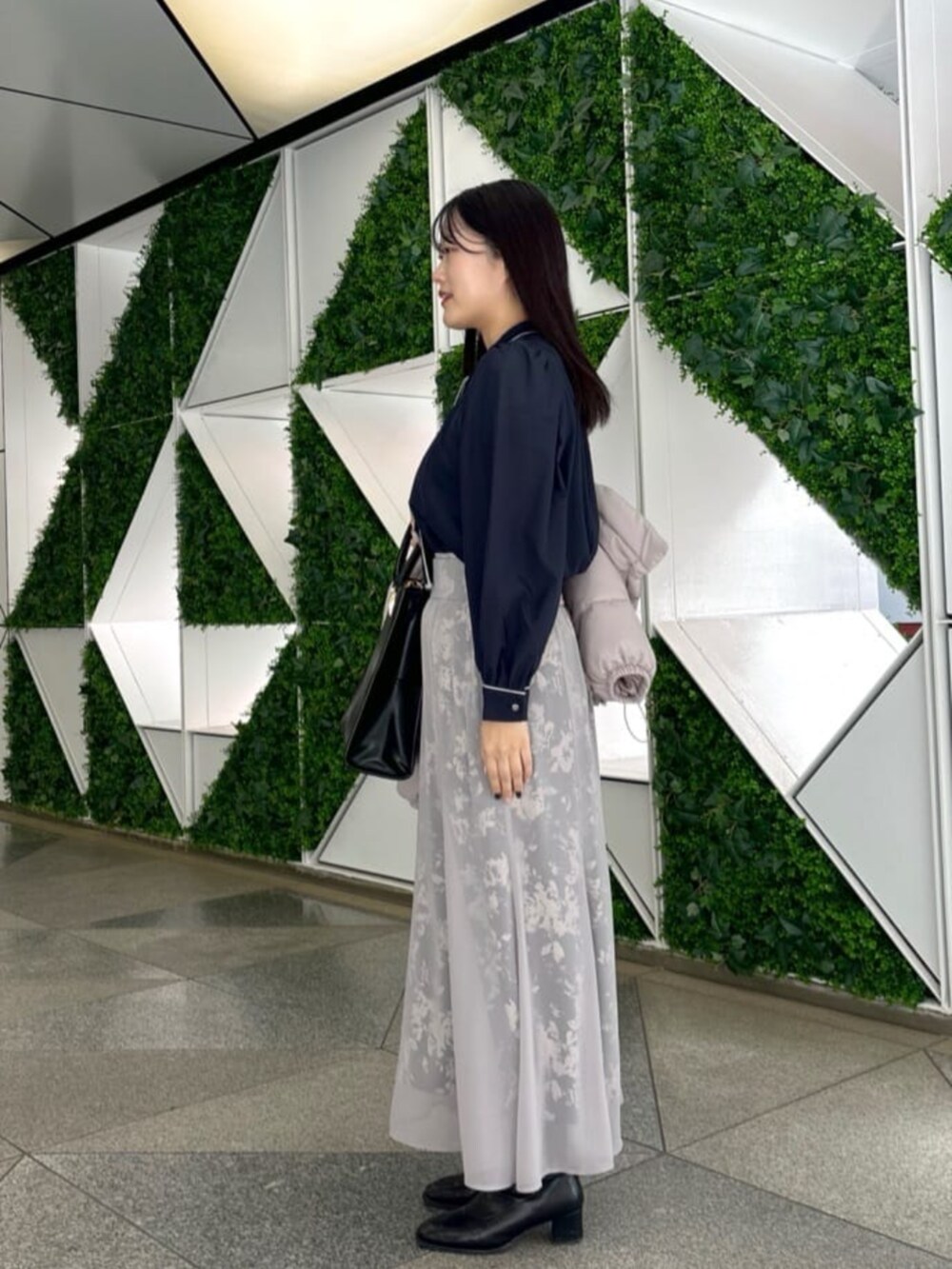 ブラック系のスカート、ベージュ系のダウンジャケット/コート、ブルー系のシャツ/ブラウスを着用したレディースの秋コーディネートの4枚目の写真