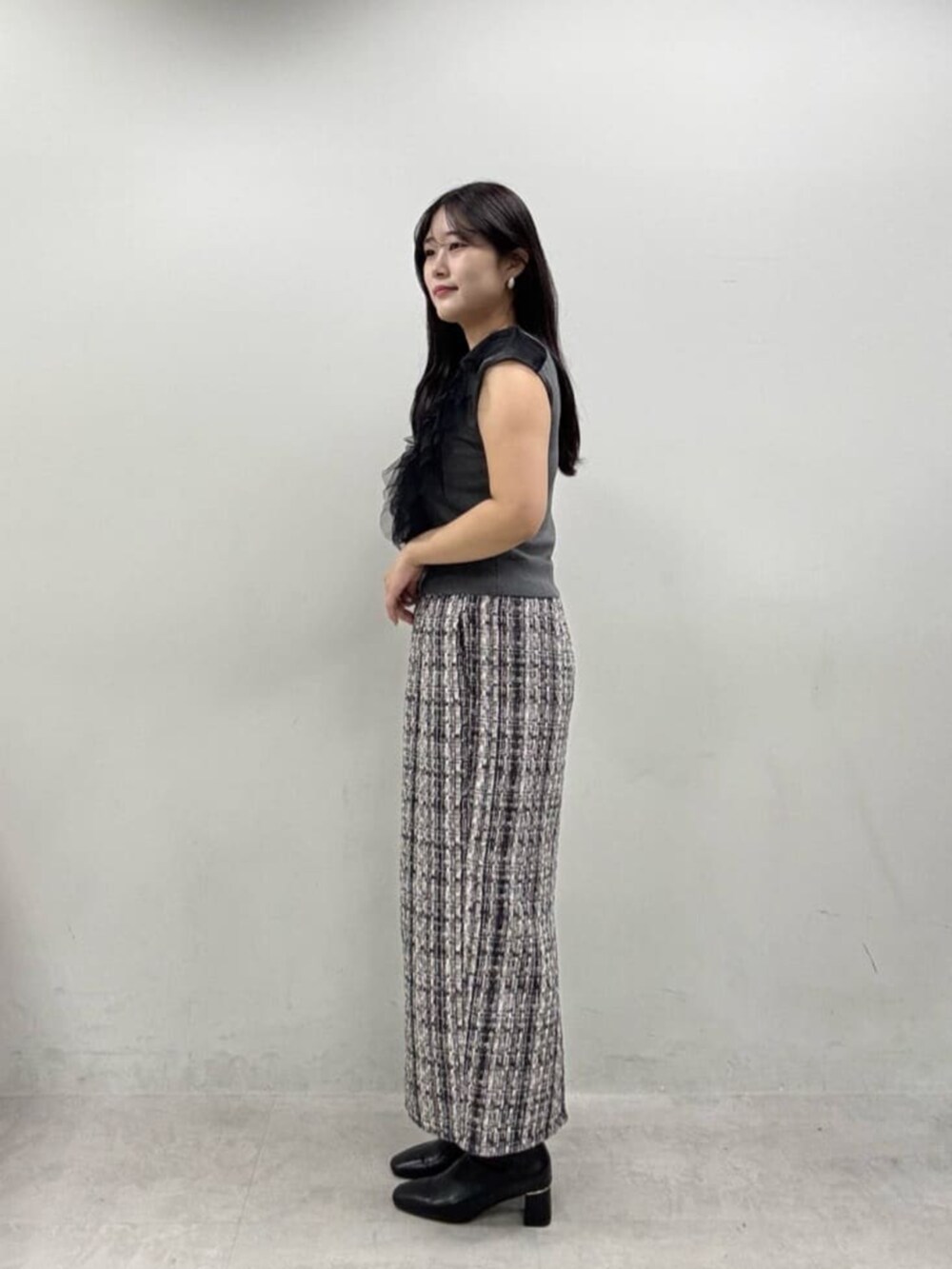 グレー系のスカート、ブラック系のブーツ、グレー系のベストを着用したレディースの秋コーディネートの2枚目の写真